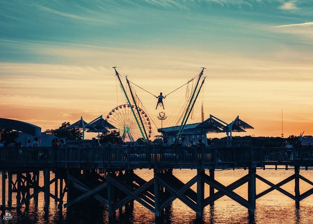 Waterfront rides and a Ferris wheel at Broadway at the Beach at sunset, photographed in June 2024